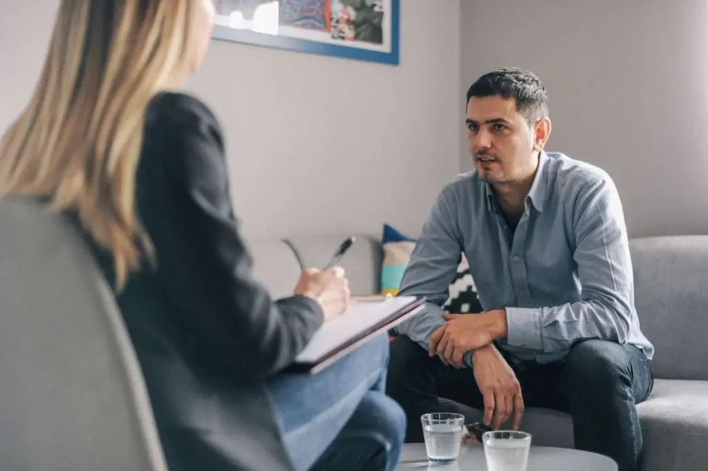 Therapy session for a male truck driver discussing CDL requirements and mental health with a psychologist.