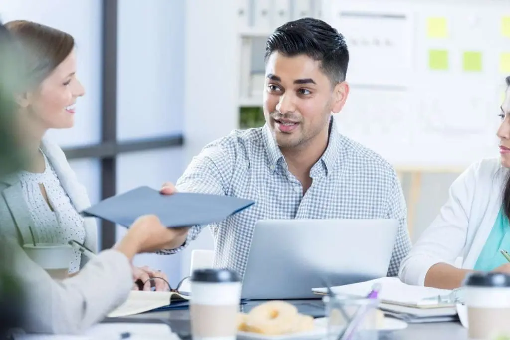 A focused man handing over a folder during a case management meeting, symbolizing the exchange of crucial information.