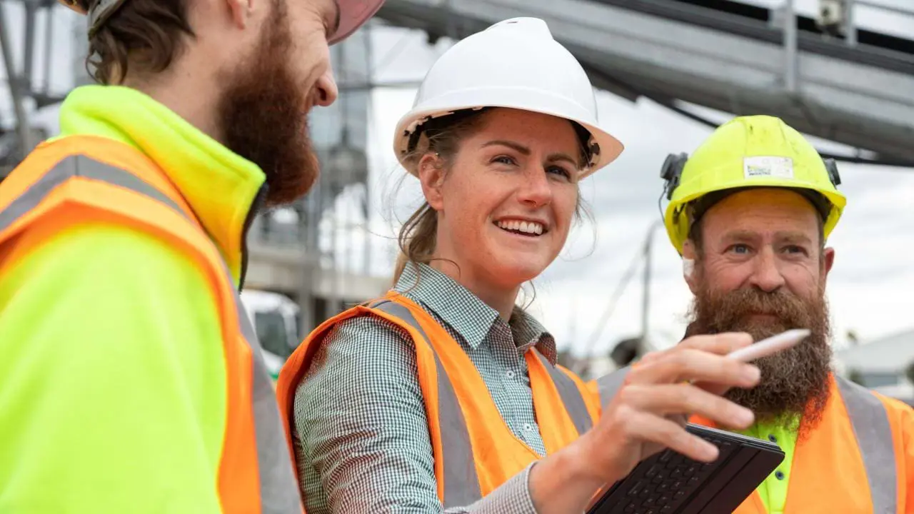 Smiling construction team in hard hats reviewing progress on tablet
