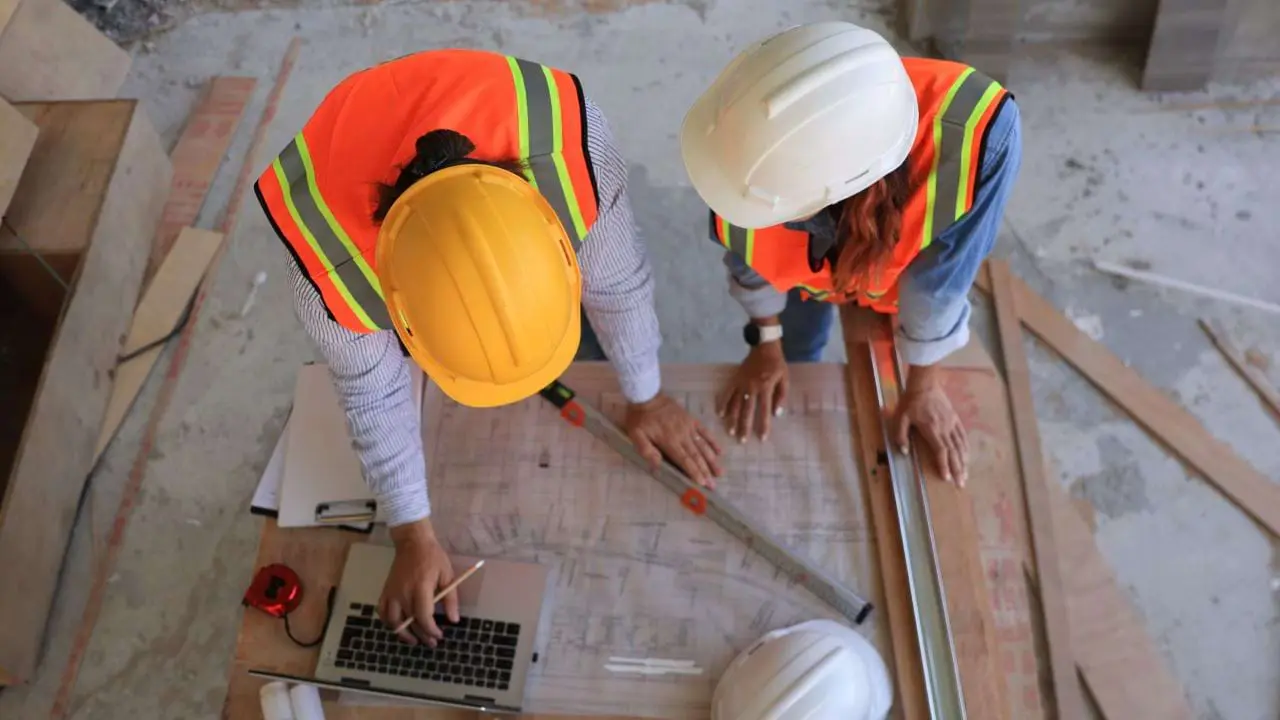 Top-down view of blueprint, ruler, and hard hats on a worktable