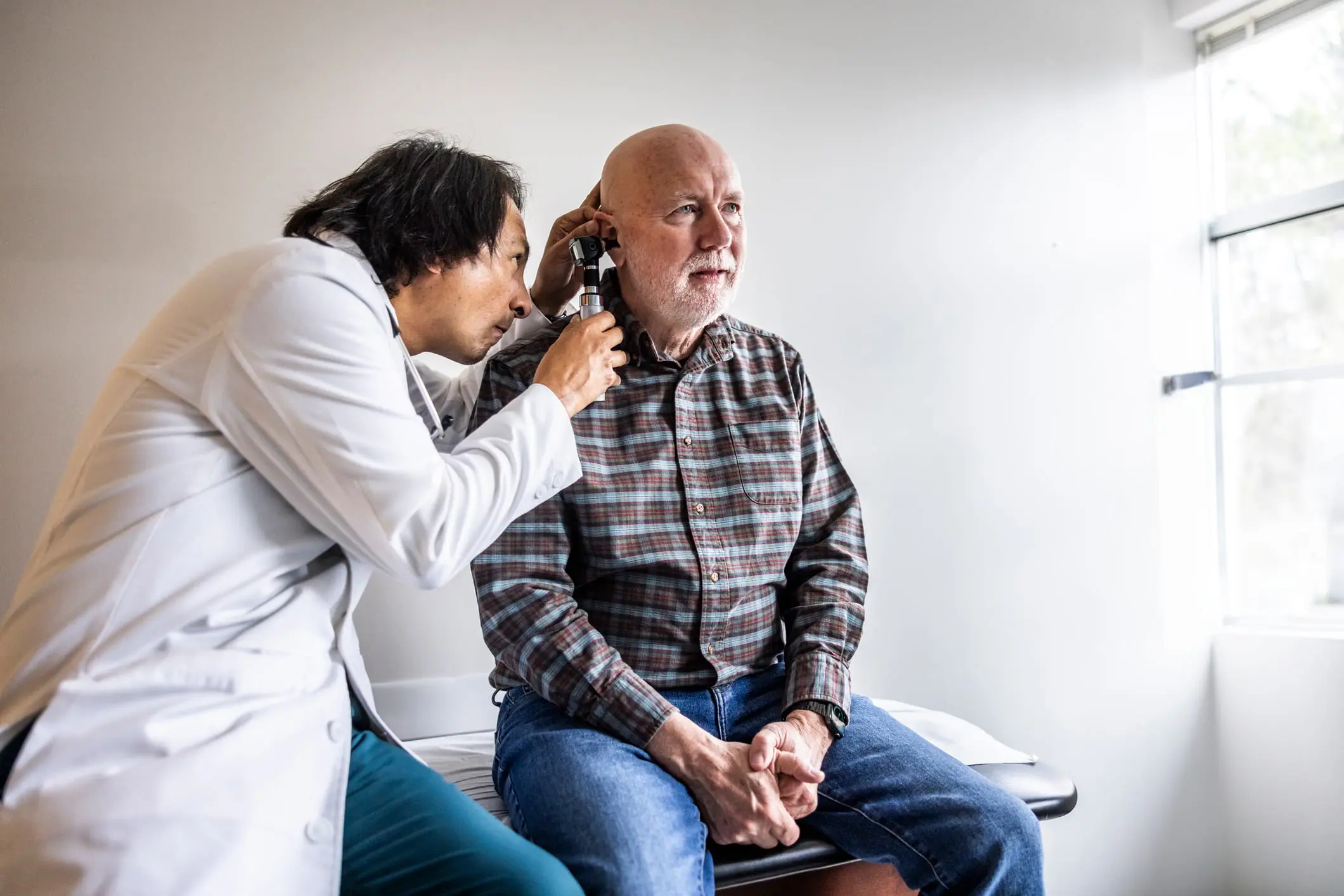 Medical examiner checking a patient’s ear during a DOT physical—ongoing monitoring to keep certification valid.