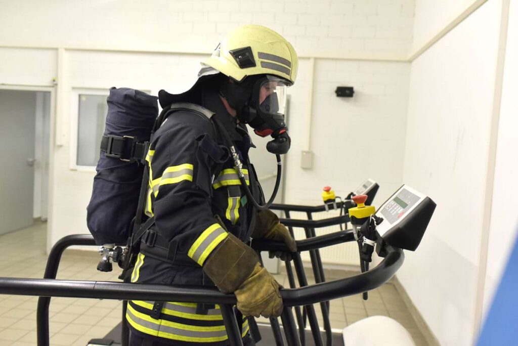 Firefighter in comprehensive protective gear, running a treadmill test, showcasing the physical demands and relevance to nfpa 1582 medication disqualifications.