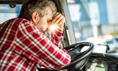 Male truck driver with mental illness hunched over steering wheel, reflecting on CDL requirements.
