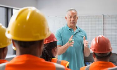 A man giving a safety briefing to workers in hard hats.