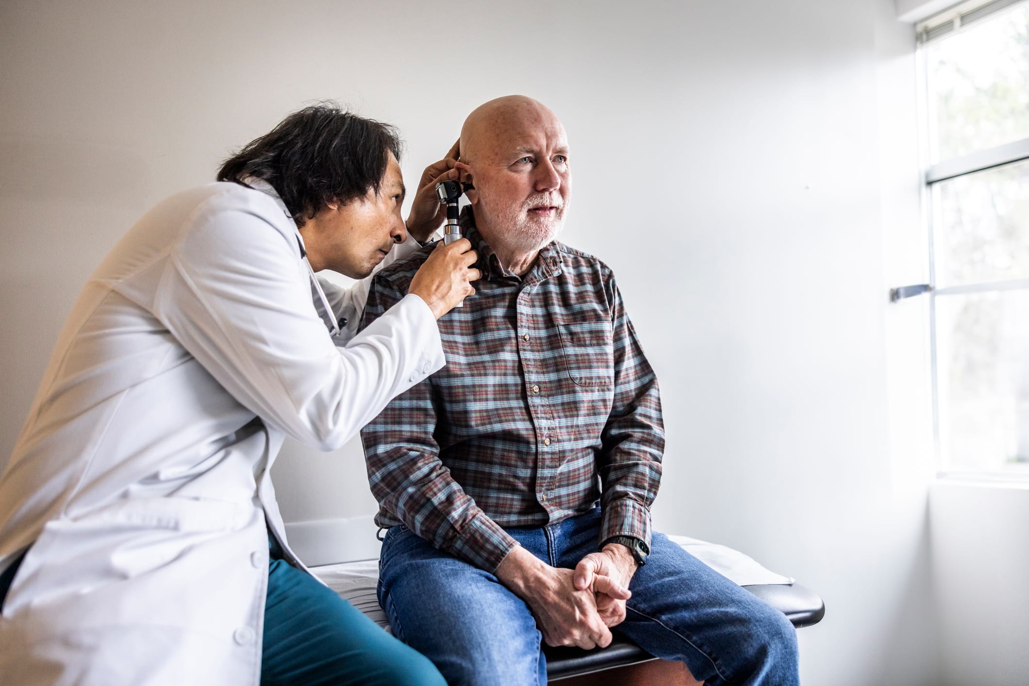 Medical examiner checking a patient’s ear during a DOT physical—ongoing monitoring to keep certification valid.